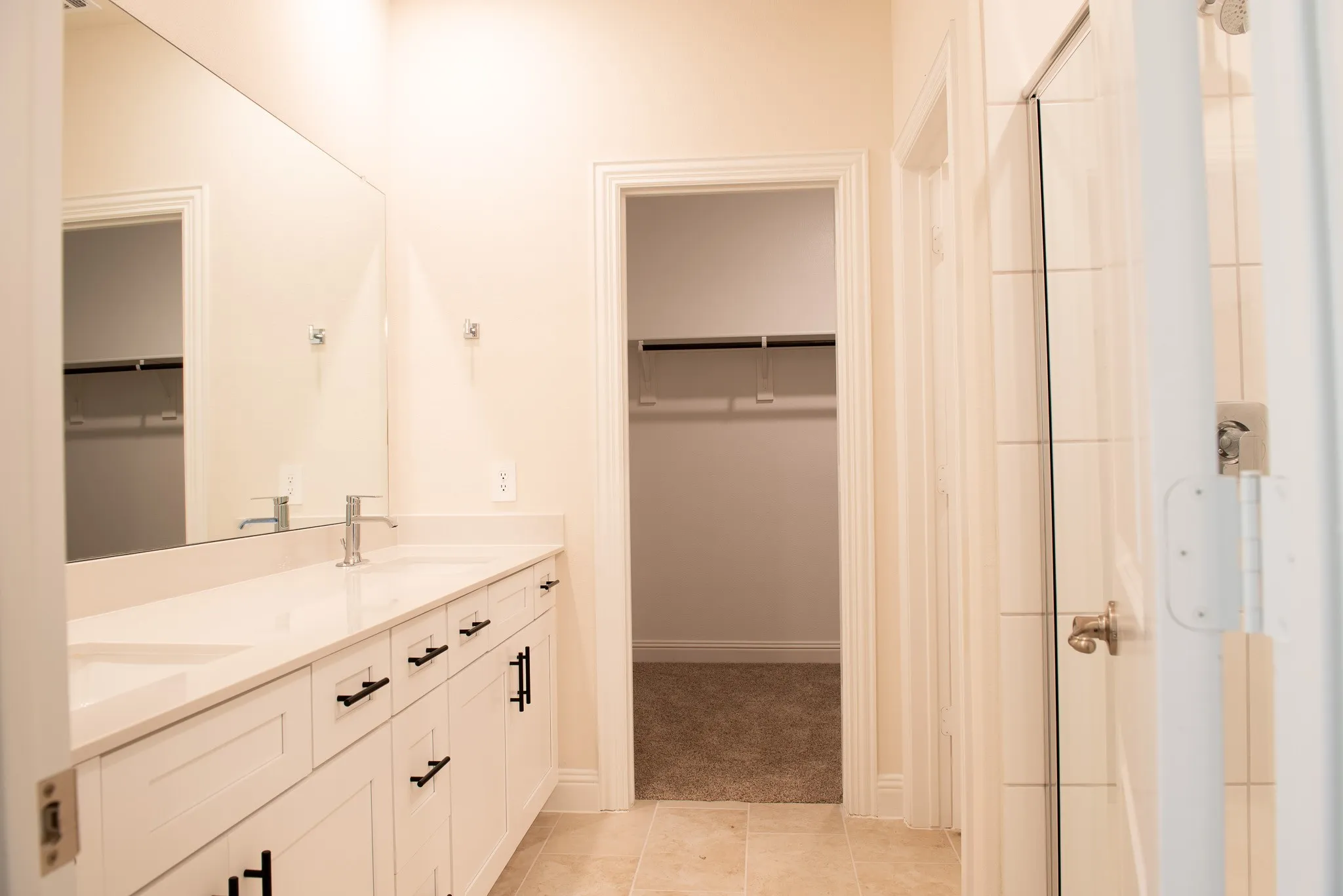  Elegant master bathroom featuring dual vanities with quartz counters, upgraded cabinetry, and walk-in shower, with direct access to a spacious walk-in closet.