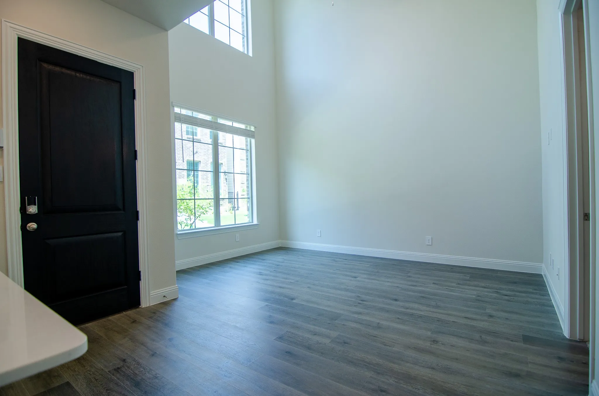 Open view from the kitchen into the living room featuring soaring ceilings, wood-look flooring, and large windows that bring in abundant natural light.