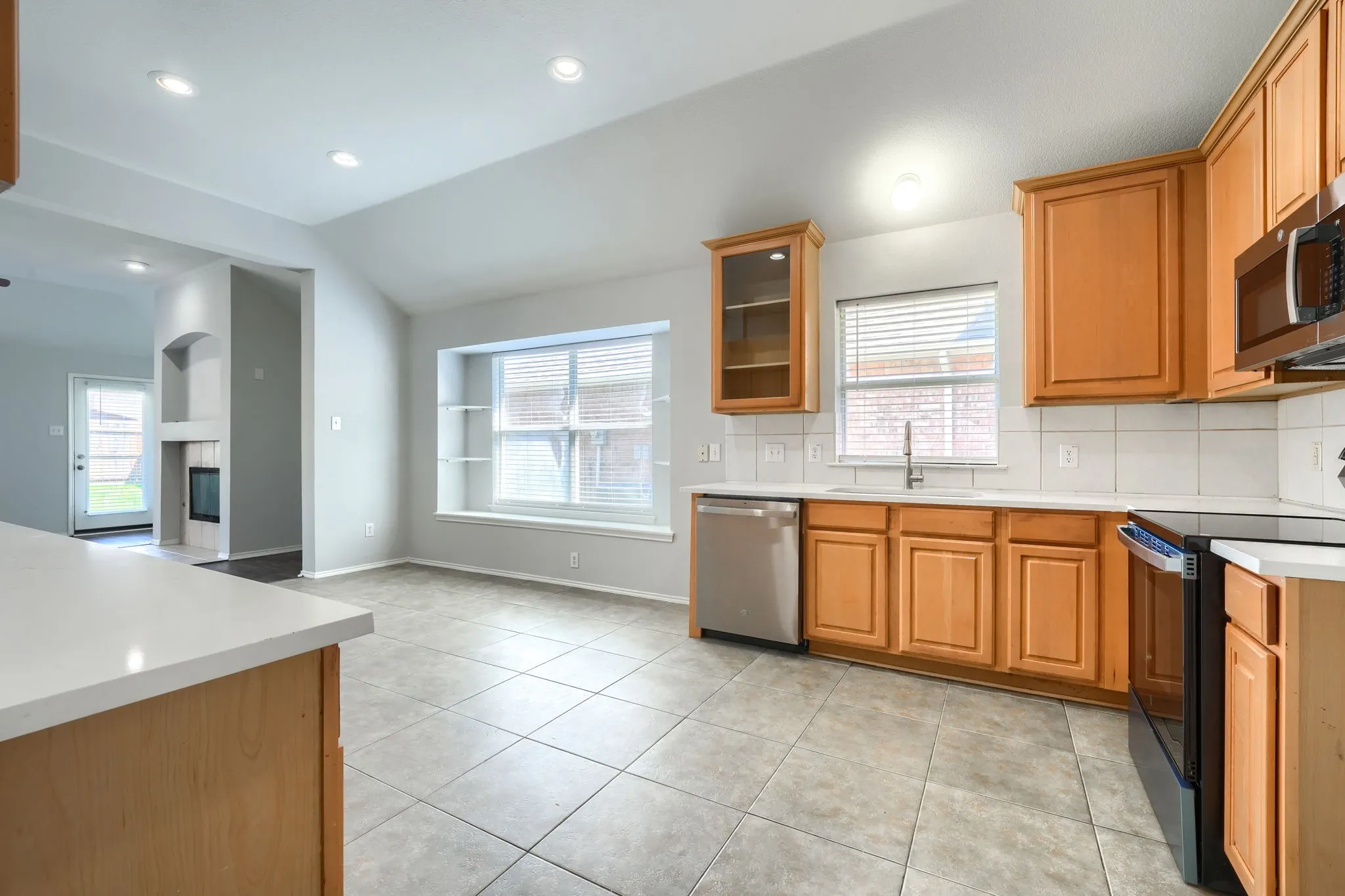 Kitchen featuring light wood-finish cabinetry, stainless steel appliances, a white tile backsplash, and light-colored countertops