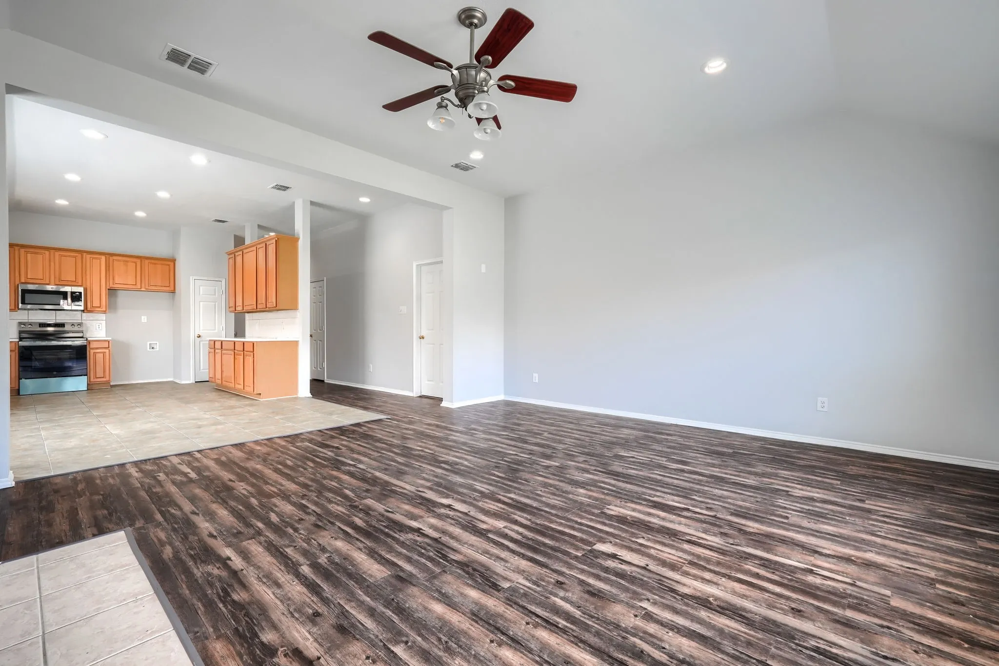 Vaulted ceiling with a ceiling fan, recessed lighting, wood-finish flooring, and kitchen with wood cabinetry
