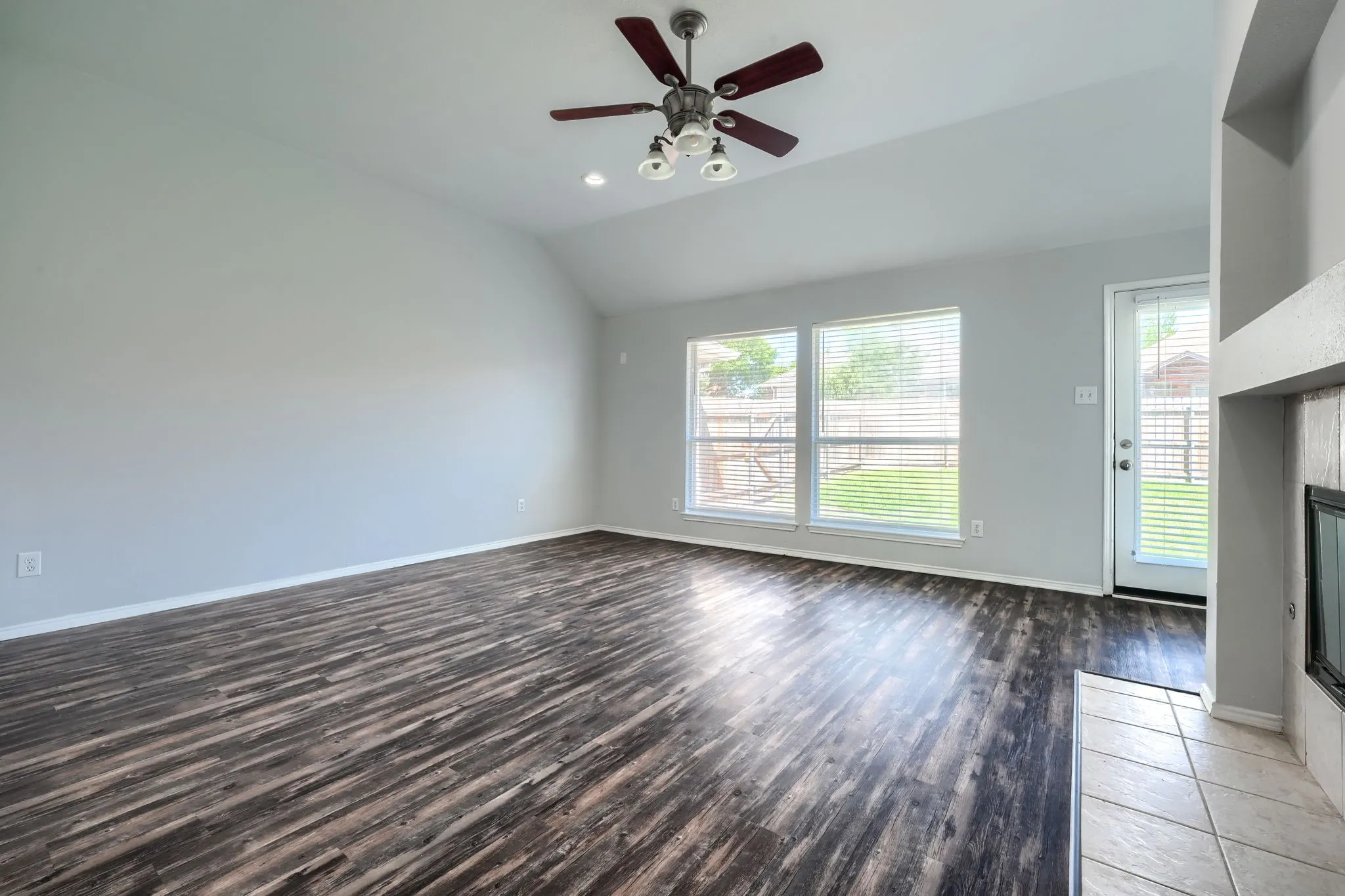 Vaulted ceiling, wood-finish flooring, ceiling fan with light fixture, multiple windows, fireplace with tile surround