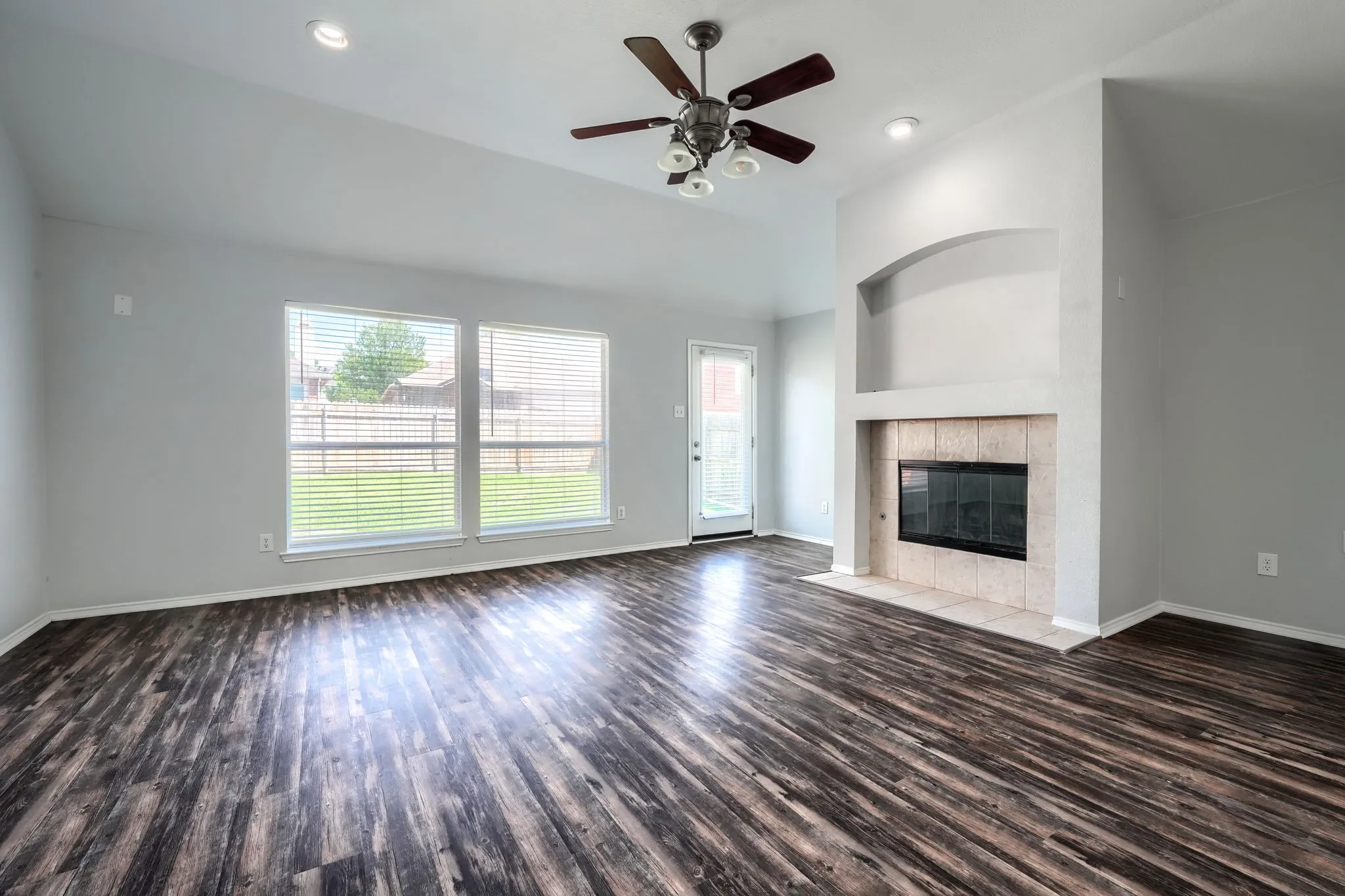Vaulted ceilings with recessed lighting, wood-finish flooring, a fireplace with a tiled surround, a built-in arched alcove, and multiple windows