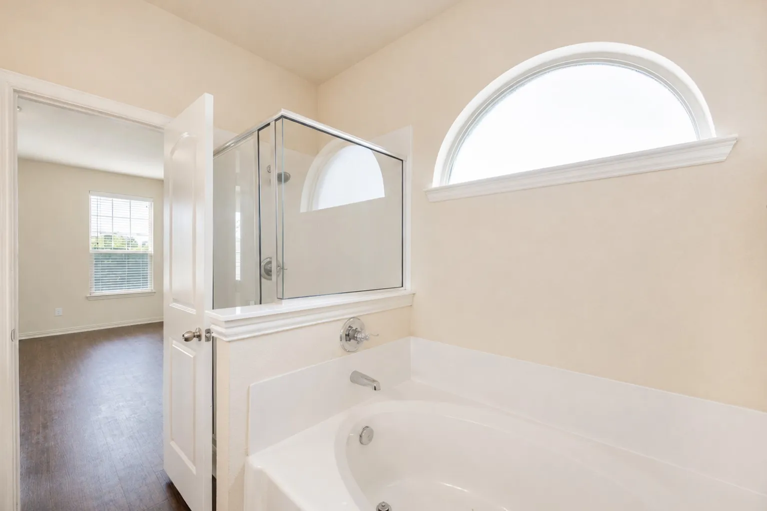 Built-in soaking tub with chrome fixtures, glass-enclosed shower, and an arched transom window