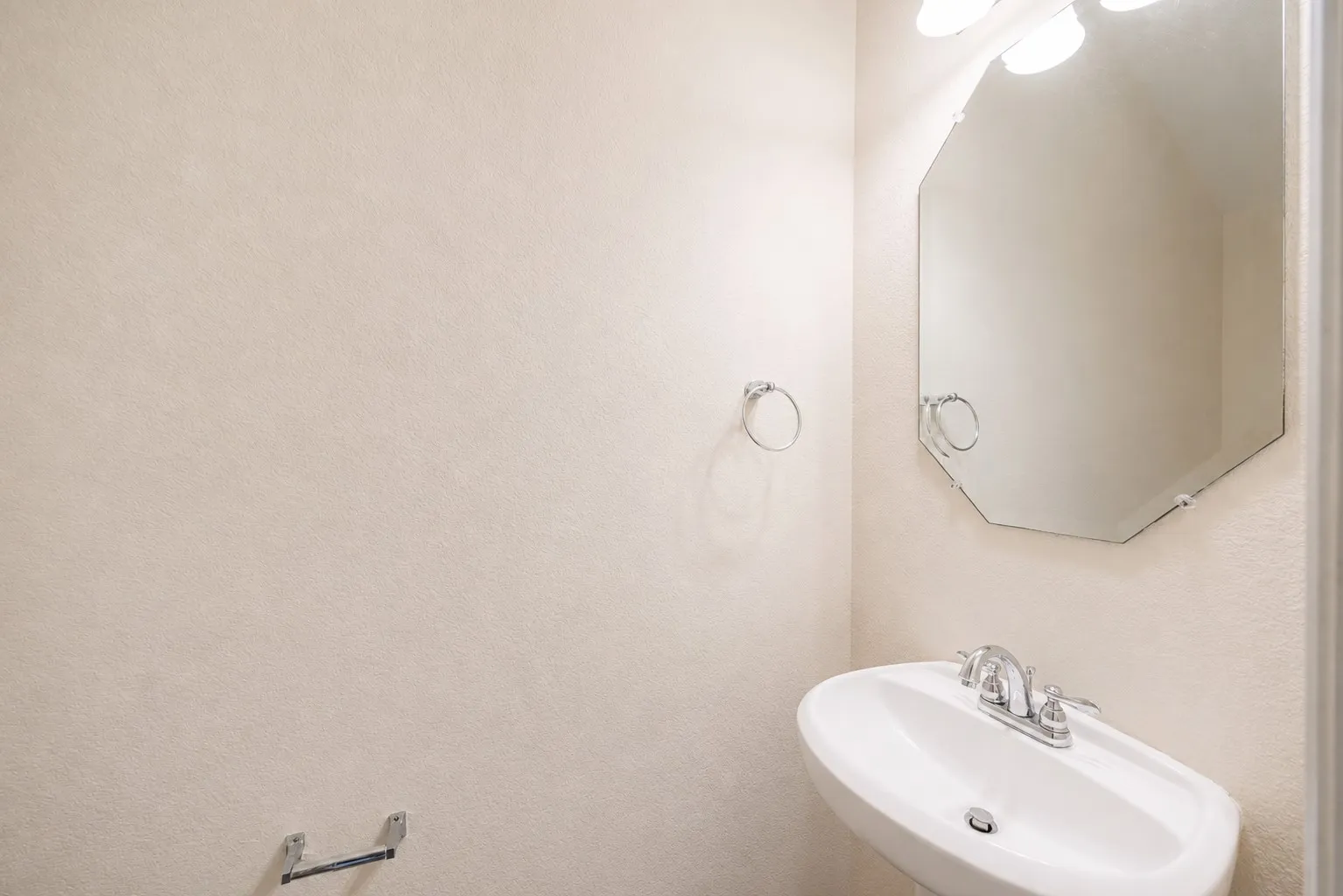 Pedestal sink with chrome faucet, octagonal wall mirror, and chrome towel ring