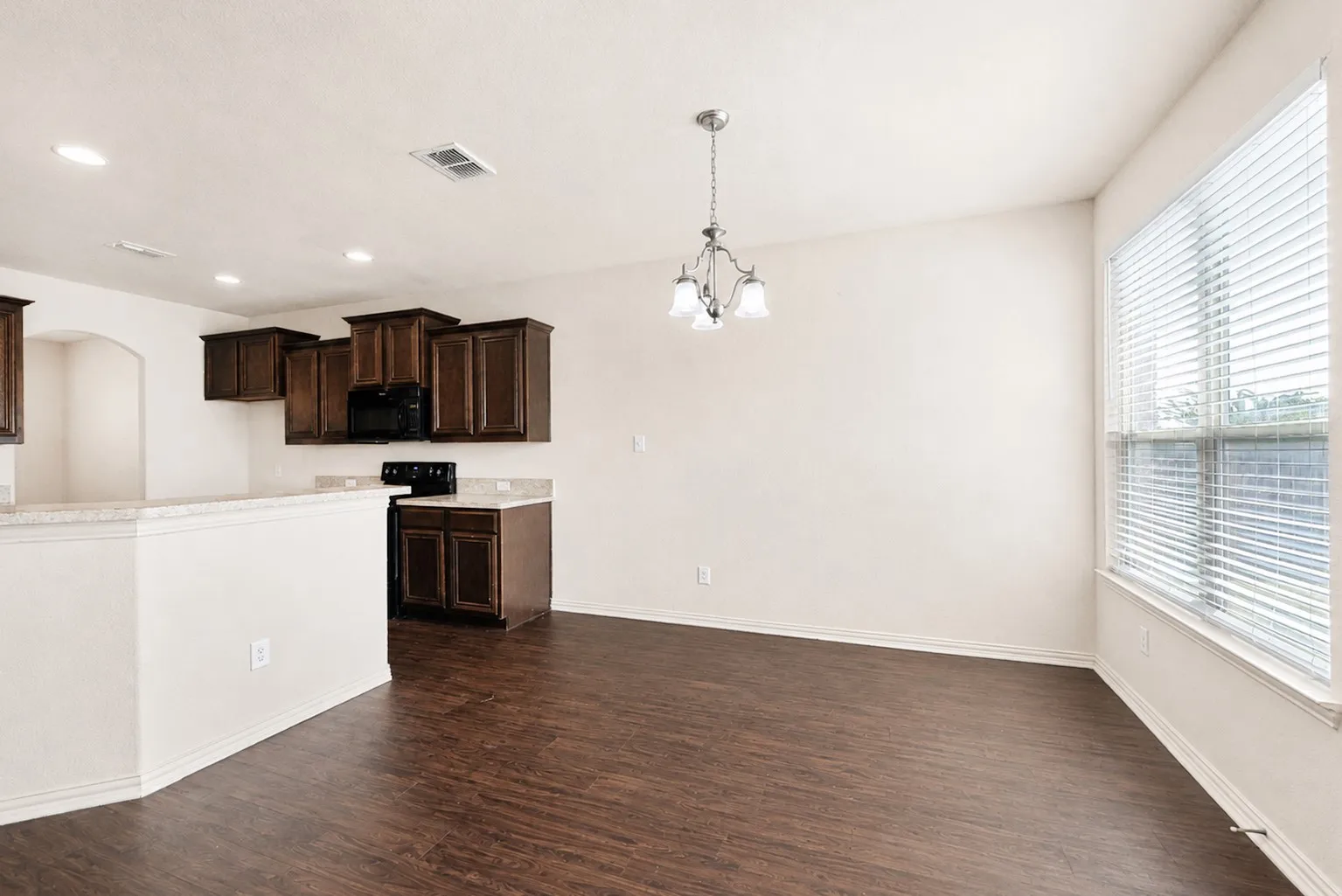 Kitchen and dining area featuring dark wood-finish cabinetry, light-colored countertops, black appliances, and recessed lighting