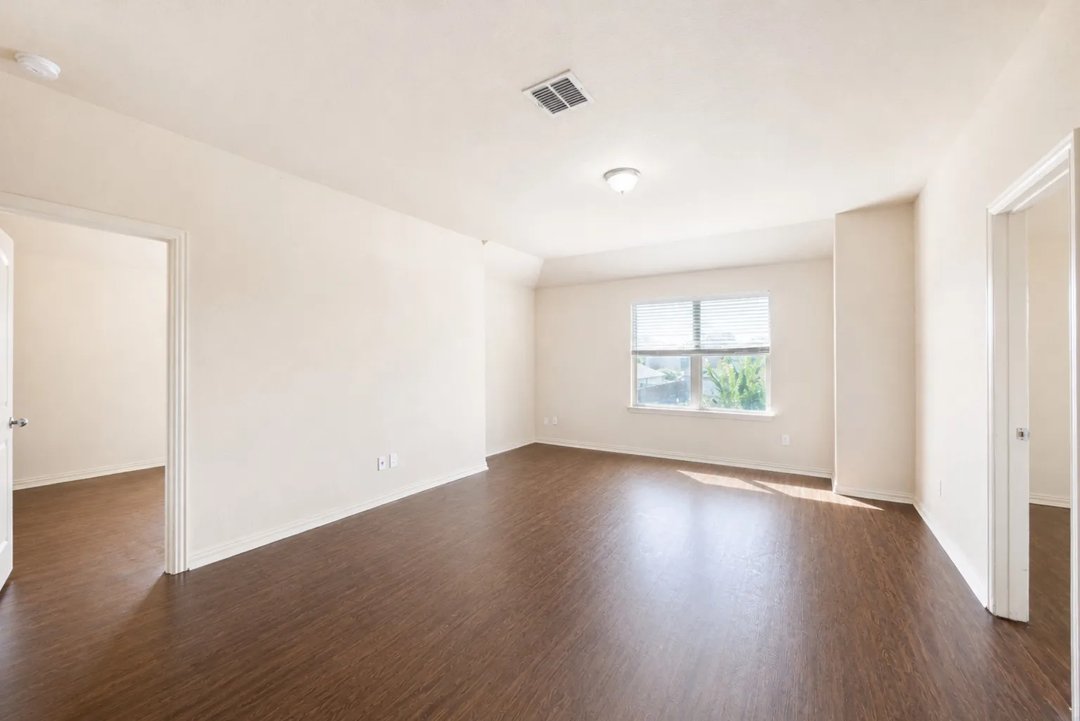 Spacious room with wood-finish flooring, neutral wall tones, and overhead lighting