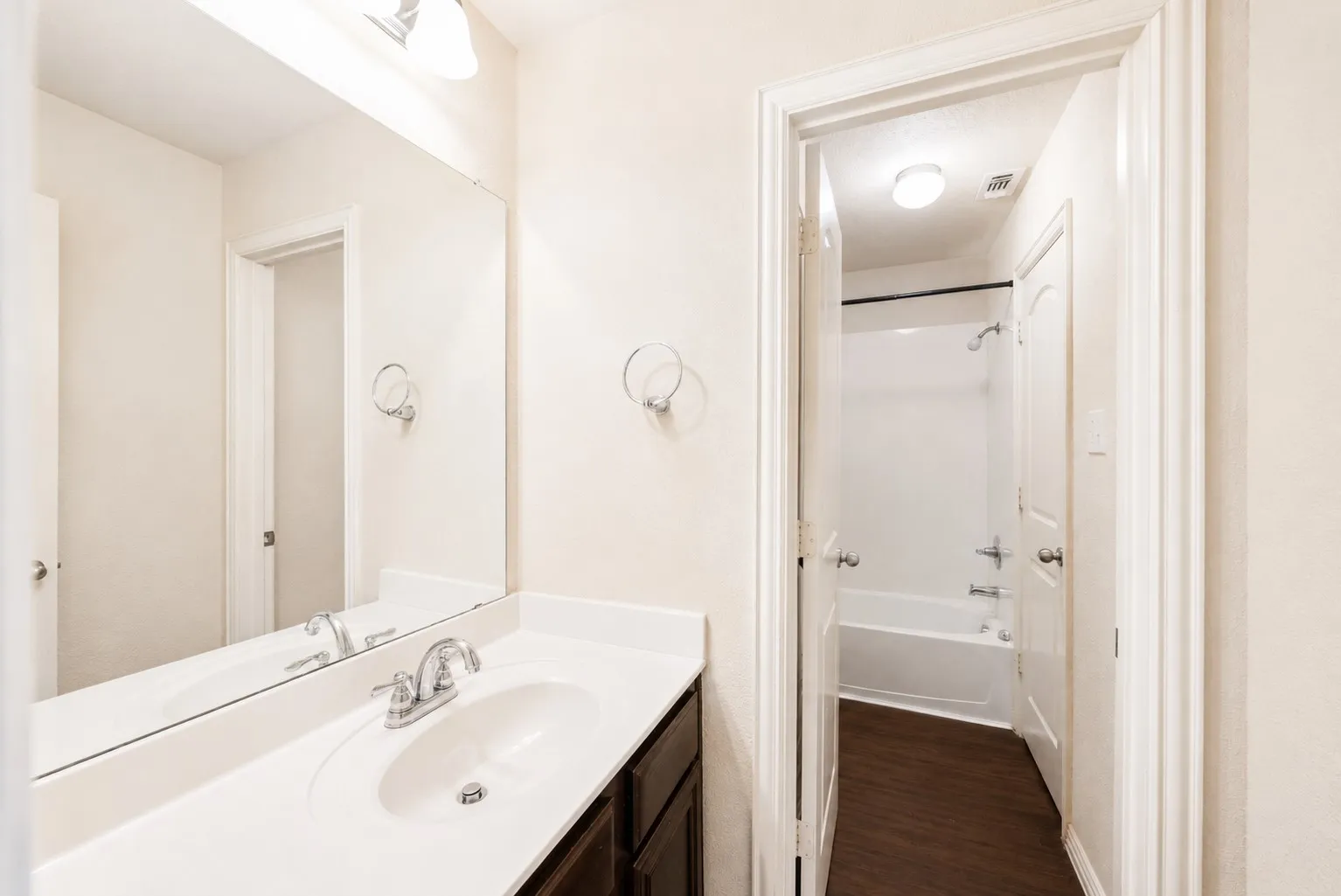 Vanity with a white countertop and integrated sink, chrome faucet, full-width mirror, and dark wood-finish cabinetry