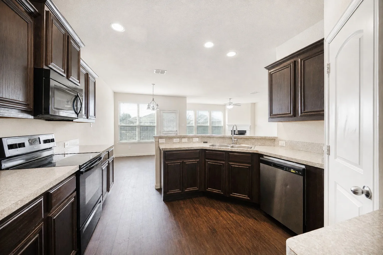 Kitchen featuring dark wood cabinetry, light-toned countertops, stainless steel appliances, and wood-finish flooring