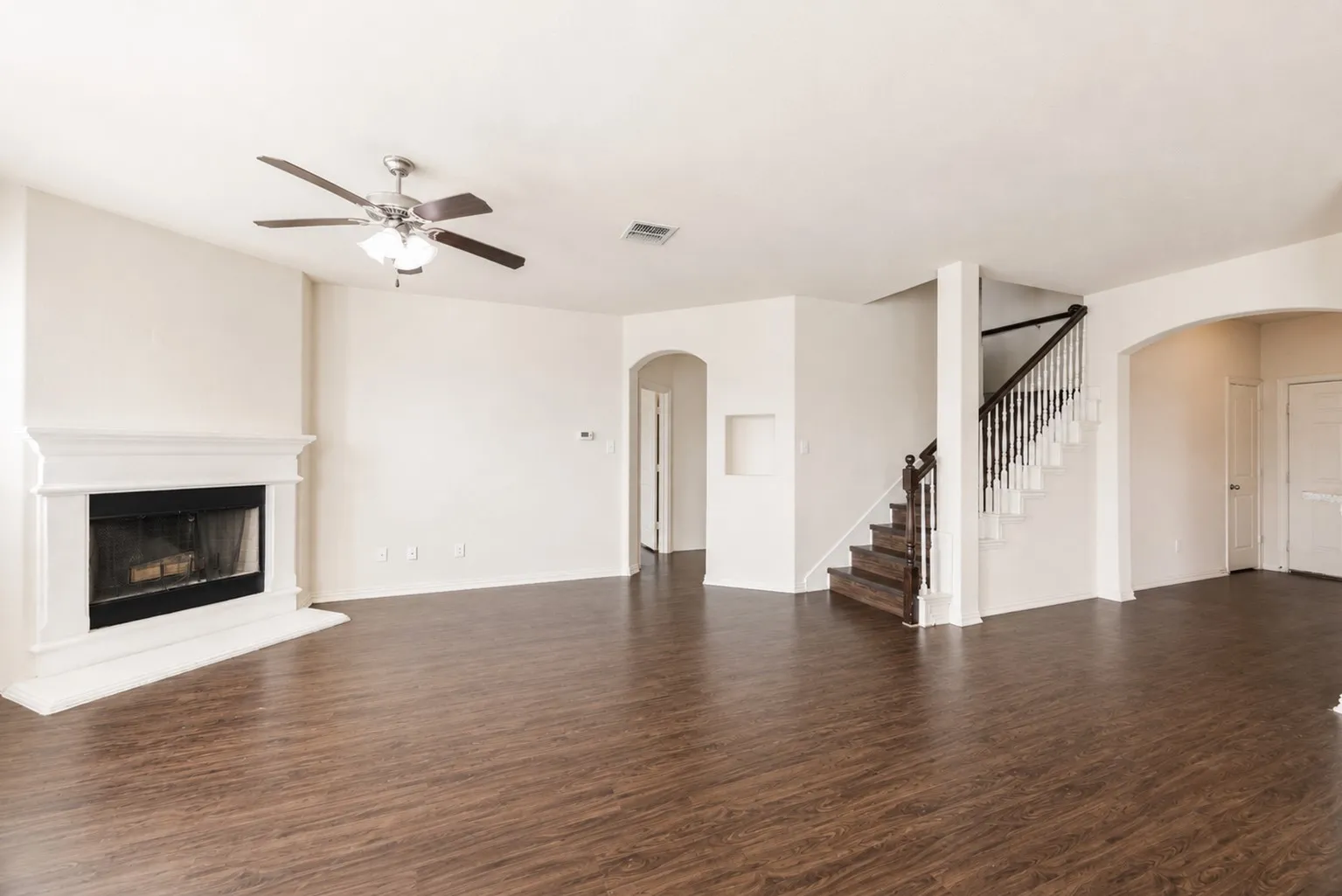 Spacious living area featuring wood-finish flooring, a traditional fireplace with a white mantel, and a ceiling fan