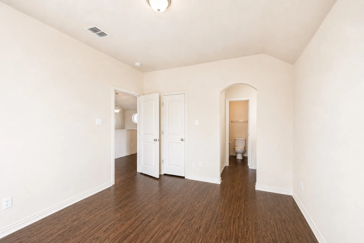 Vaulted ceiling, wood-finish flooring, white walls, arched doorway, and interior doors