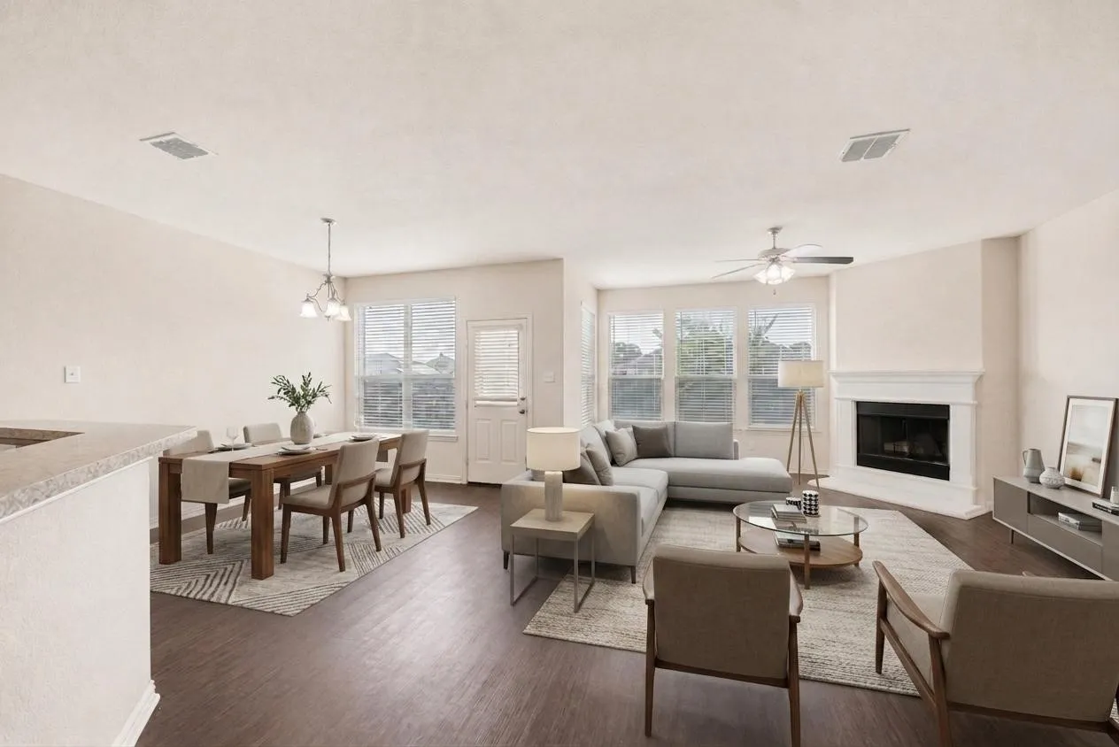 Wood-finish flooring throughout, a dining area with pendant lighting, a living area with a fireplace, multiple windows with blinds, and a ceiling fan