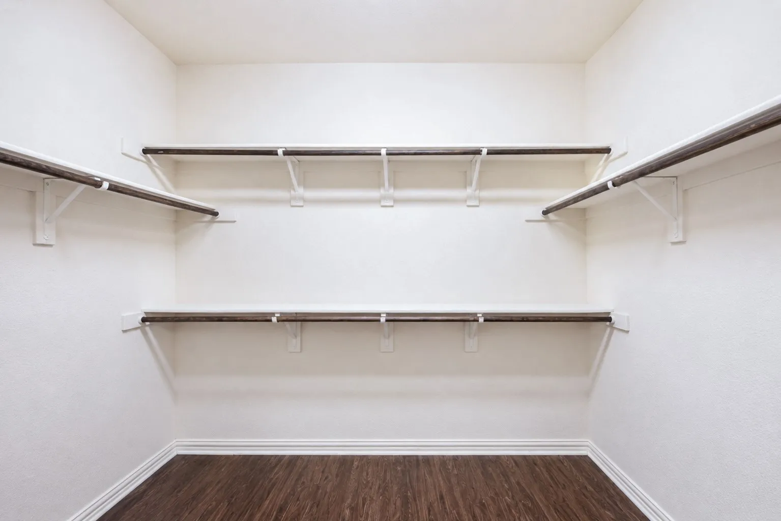Walk-in closet with wood-finish flooring, white walls, and built-in shelving with hanging rods