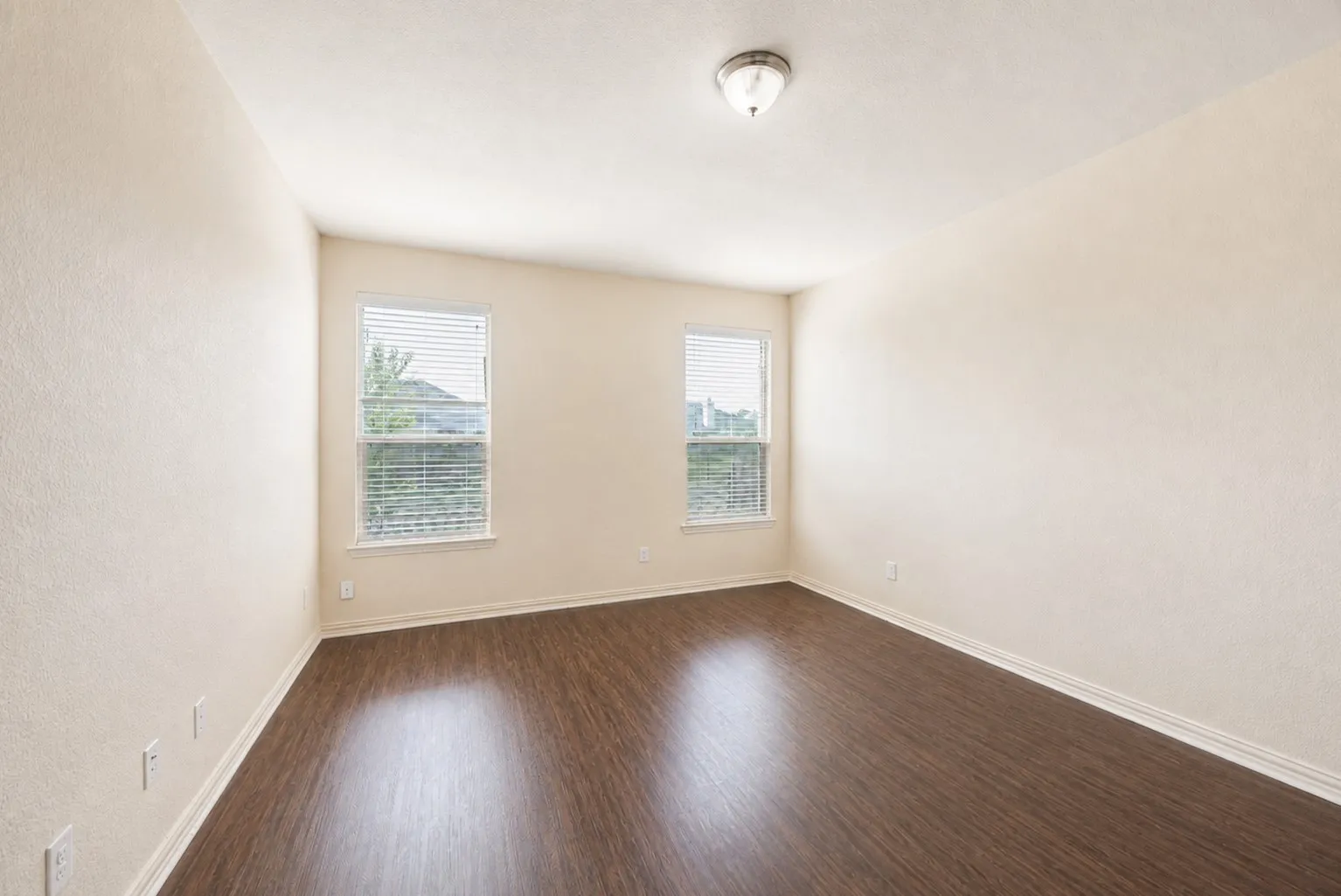Wood-finish flooring, two windows with blinds, a ceiling-mounted light fixture, and neutral wall tones