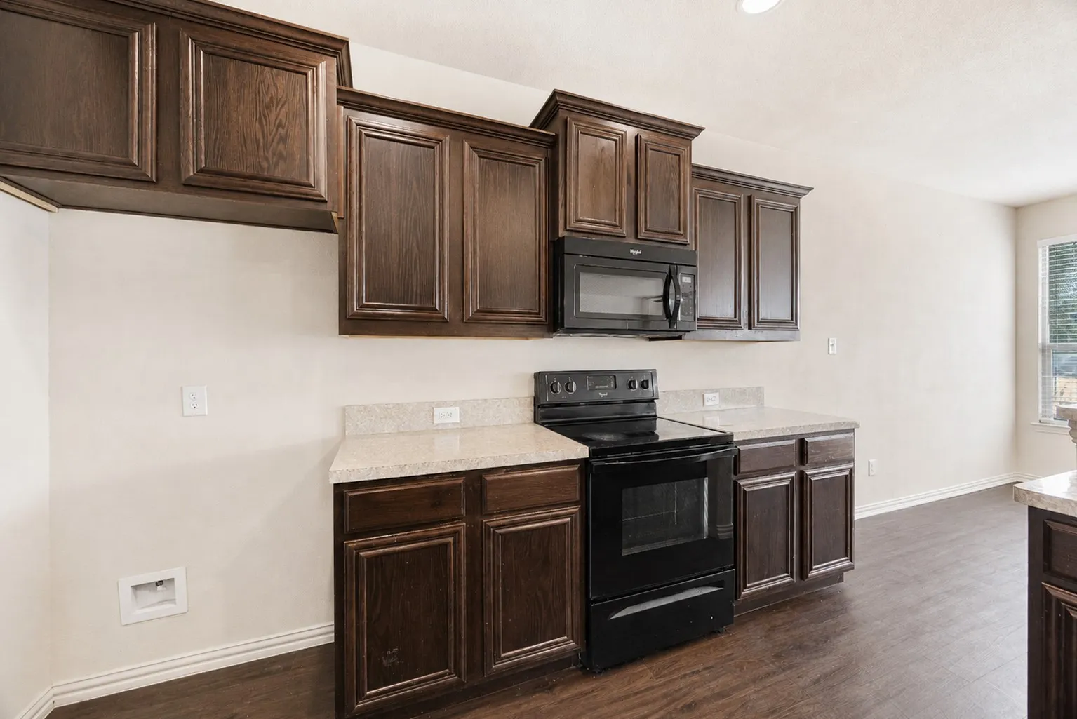 Dark wood-finish cabinetry, light speckled countertops, black electric range with matching microwave, and wood-finish flooring