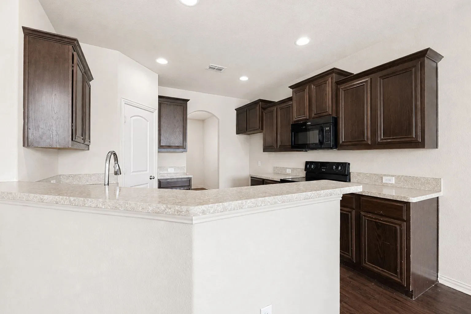 Dark wood-finish cabinetry, light-toned countertops, built-in microwave, and electric range
