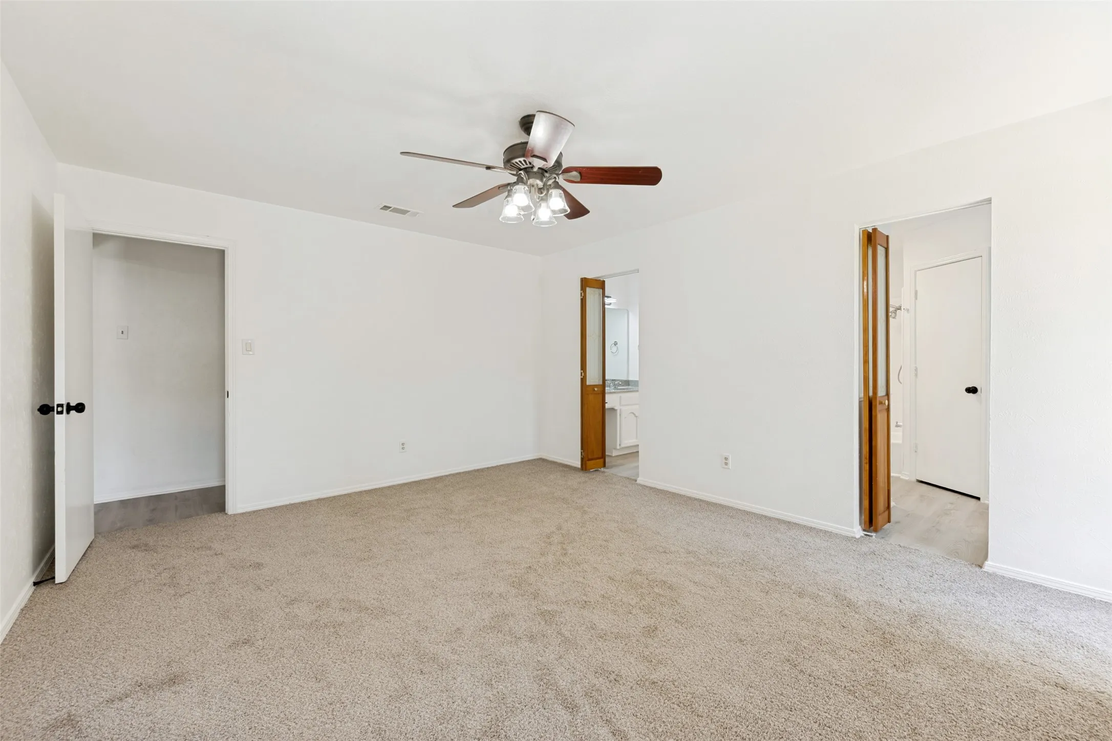Neutral tone wall paint, neutral tone carpeting, ceiling fan with light fixture, wood-finish bi-fold door, recessed closet
