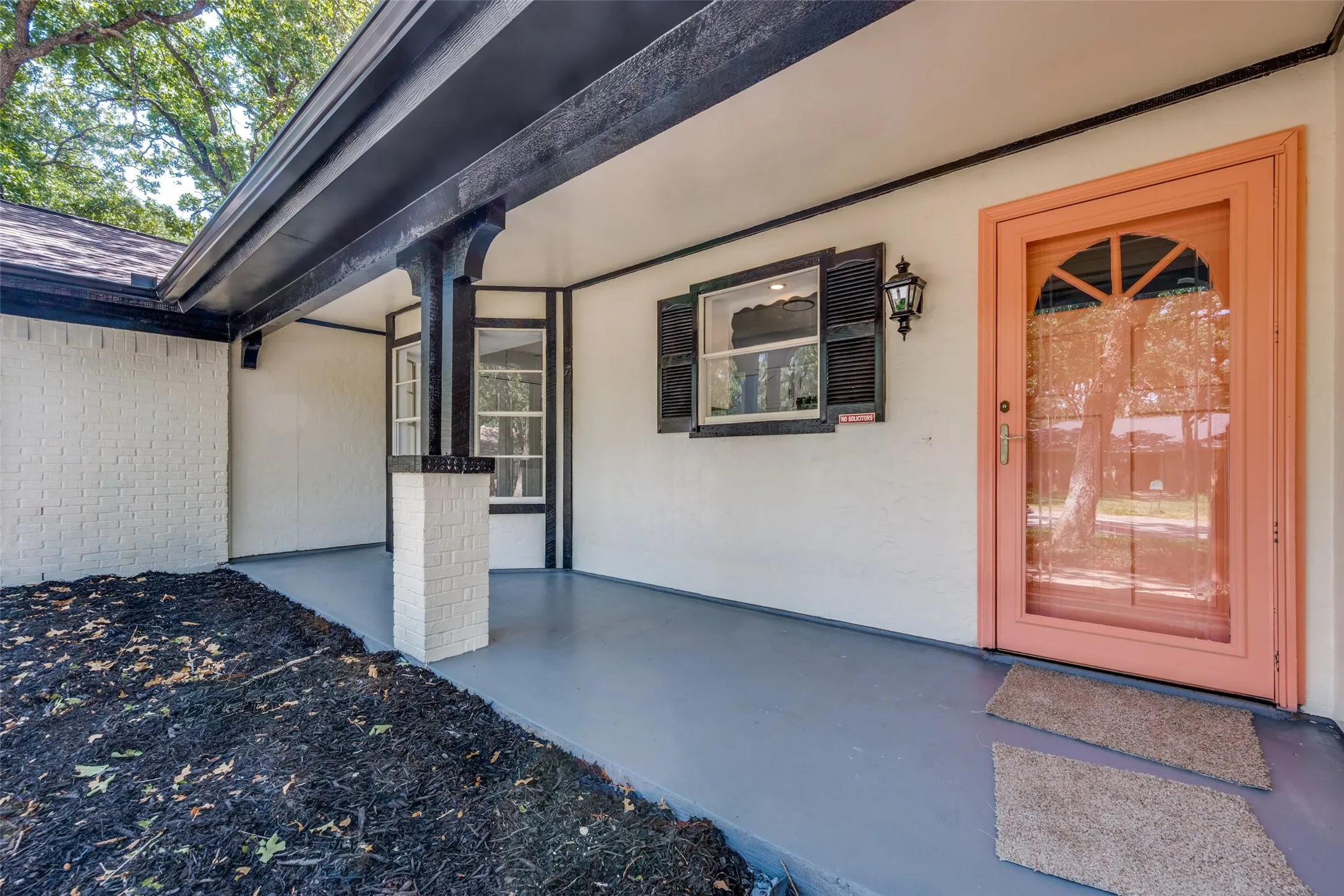 Covered front porch with painted concrete floor, brick column, and a pink front door