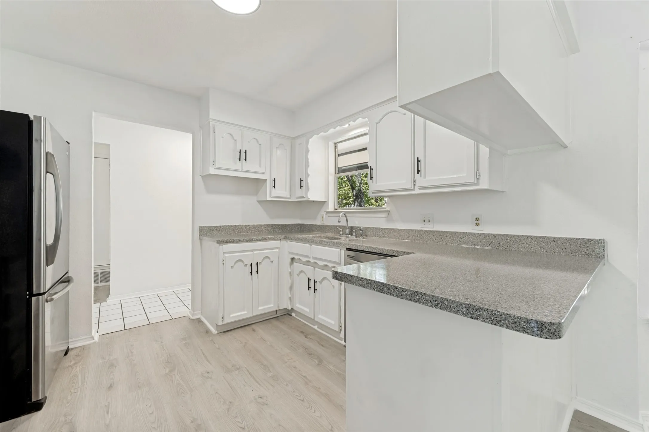 White cabinetry with dark hardware, stone-finish countertops, wood-finish flooring, and a stainless steel refrigerator