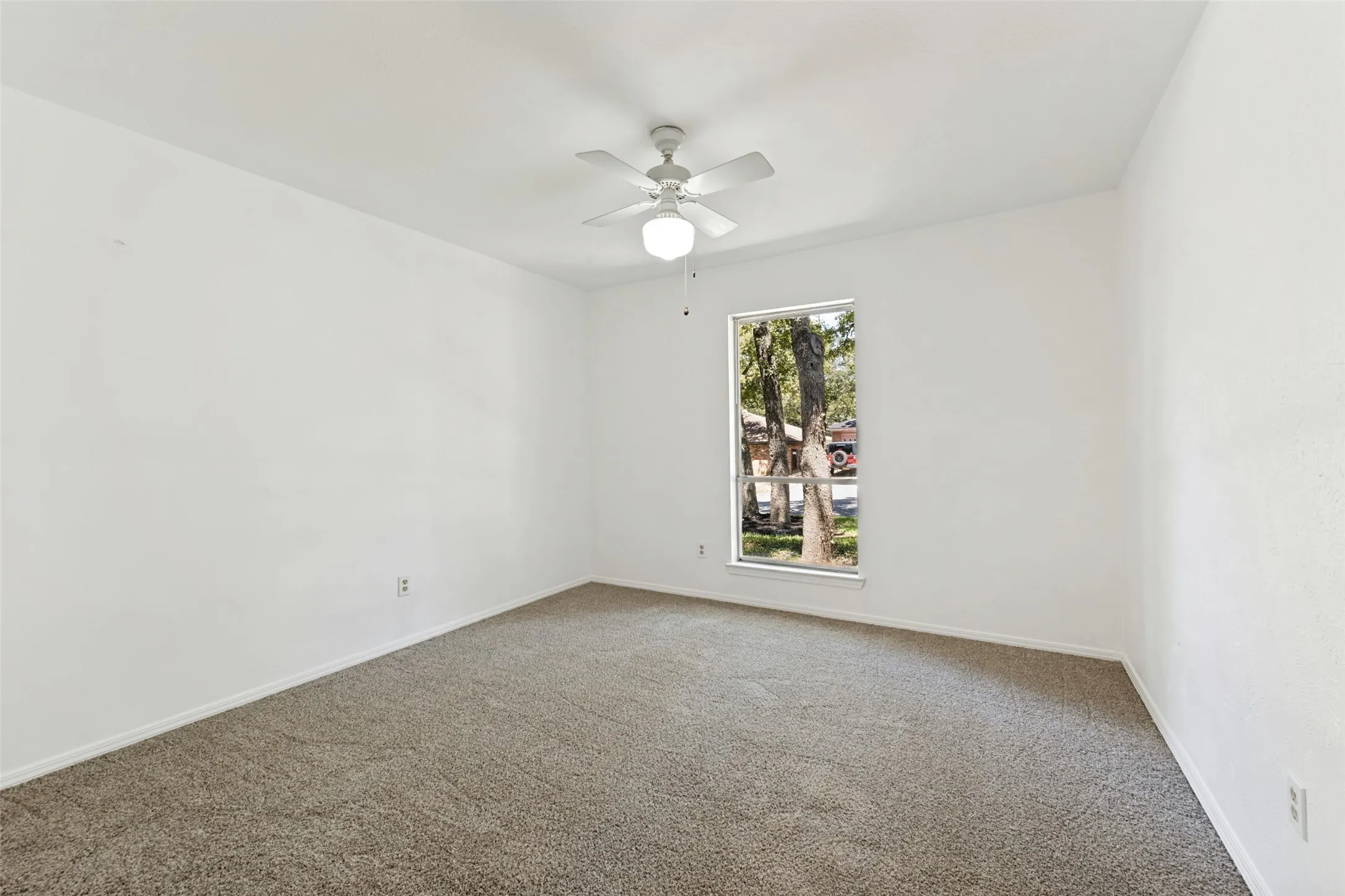 Carpeted flooring, a window with exterior scenery, a white ceiling fan with integrated lighting, and white walls