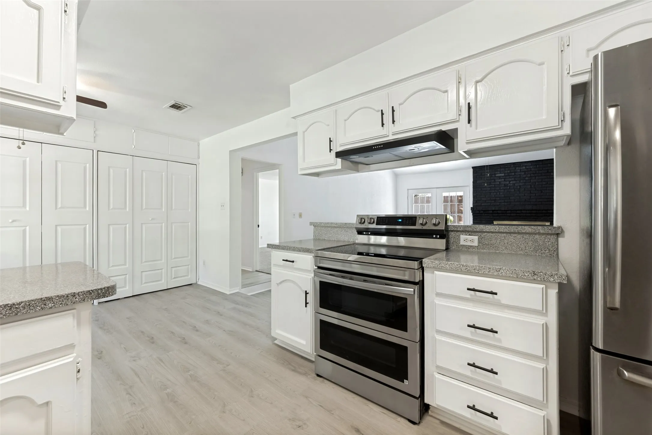 White cabinetry, stainless steel appliances, light wood-finish flooring, and grey countertops
