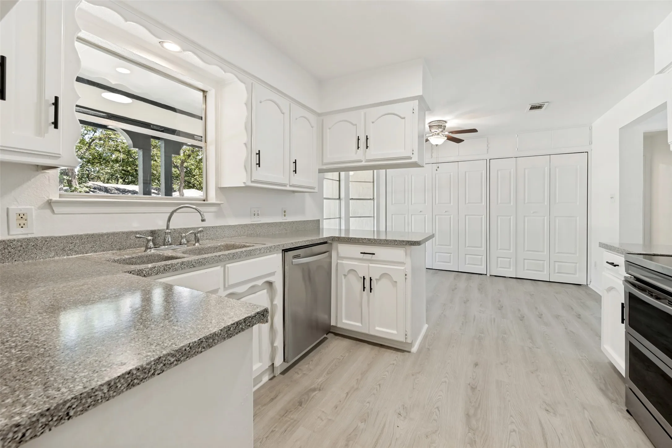 White cabinetry with black hardware, double basin sink with chrome faucet, stainless steel dishwasher, light wood-finish flooring, and white bifold closet doors