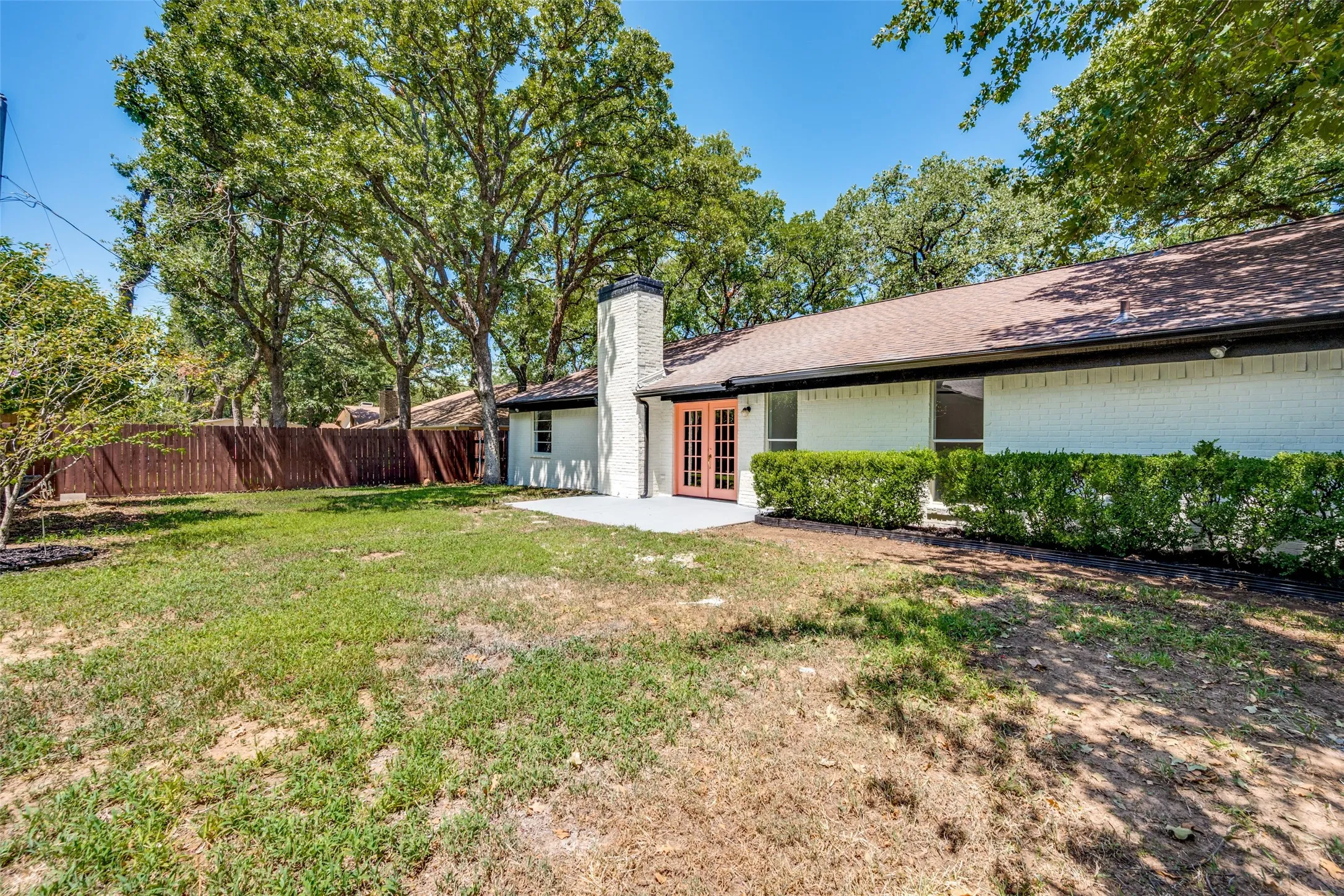Spacious backyard featuring a privacy fence, mature trees, and a patio area