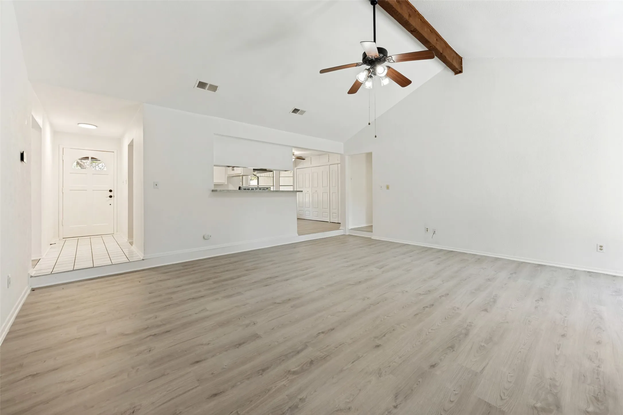 Vaulted ceiling with exposed wood beam, wood-finish flooring, ceiling fan with light fixture, and an entry door with decorative glass