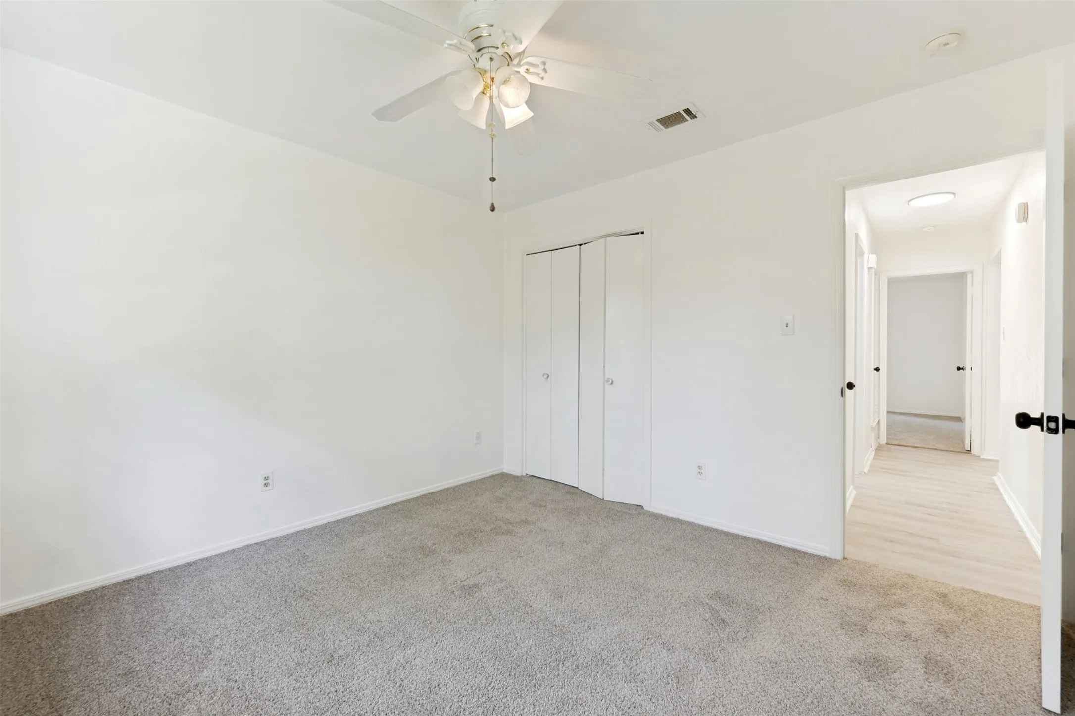 Plush gray carpeting with light-toned walls, featuring a ceiling fan with light fixture