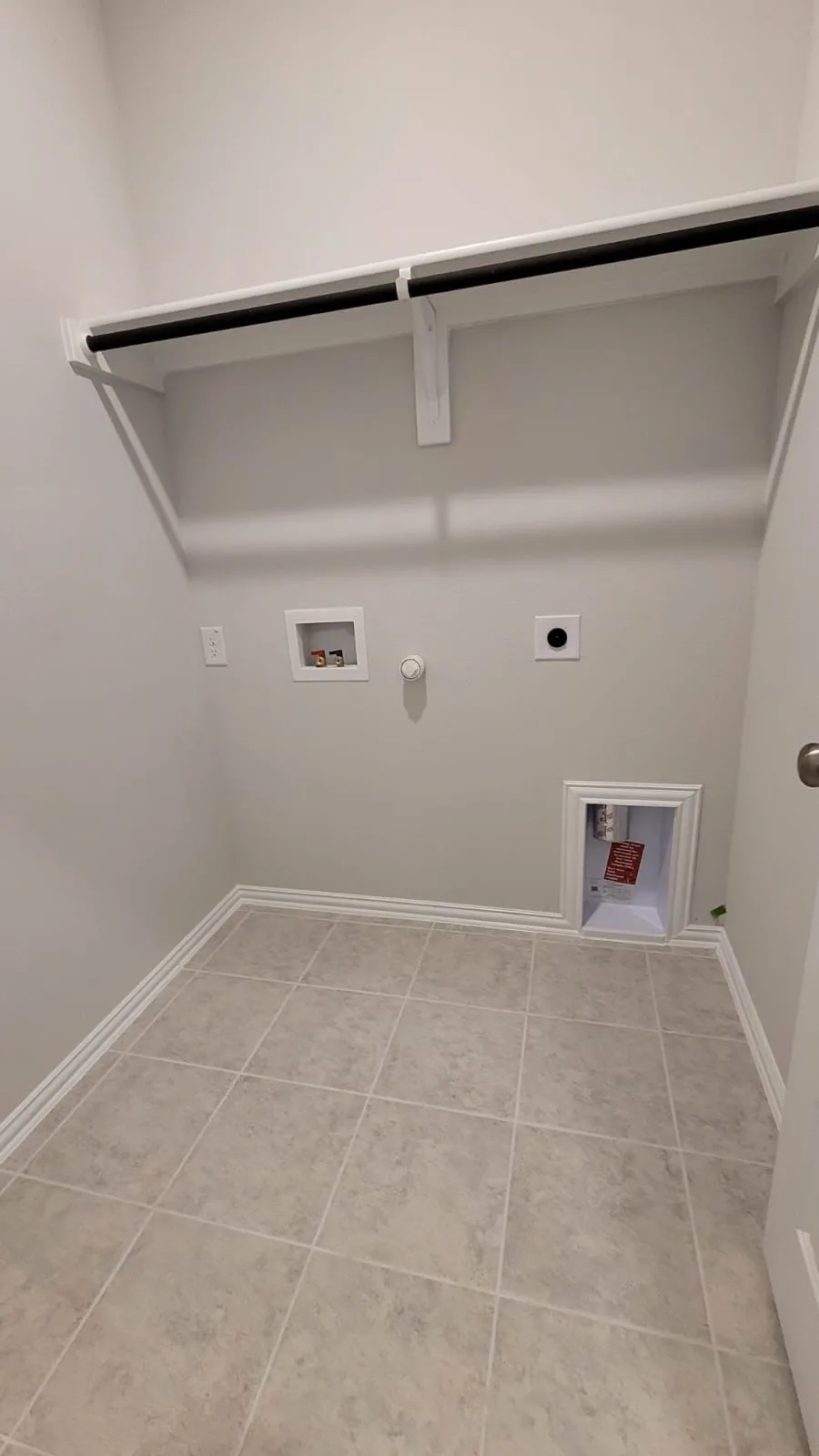 Wall-mounted shelving unit with a hanging rod, tile flooring, and white trim
