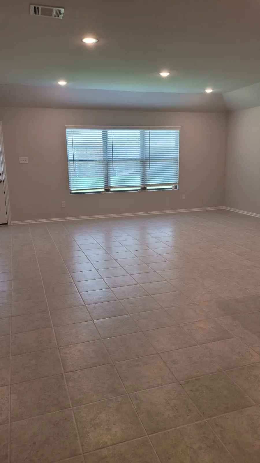 Expansive room featuring large format tile flooring, recessed ceiling lighting, and a window with horizontal blinds