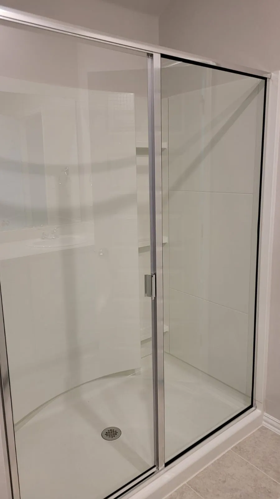 Glass-enclosed shower with a sliding door, light-colored shower base, and integrated shelving