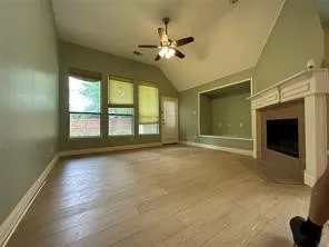 Vaulted ceiling, wood-finish flooring, built-in fireplace with mantel, recessed wall alcove, and ceiling fan