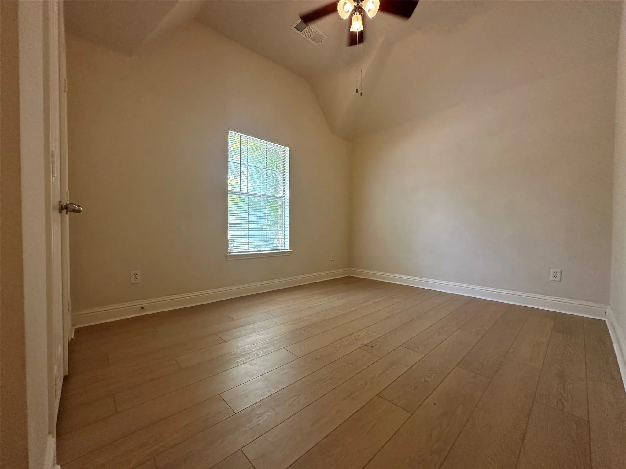 Vaulted ceiling with a ceiling fan light fixture, wood-finish flooring, white trim, and a window