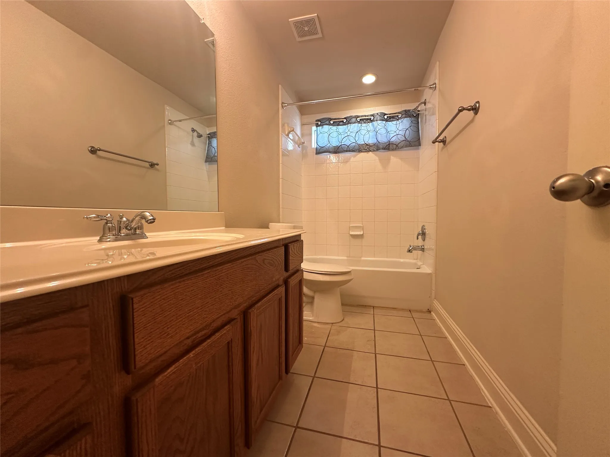 Vanity with wood-finish cabinetry and integrated sink, full-width mirror, white tiled shower and tub combination, recessed lighting, and tiled flooring
