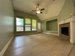 Vaulted ceiling, wood-finish flooring, fireplace with mantel, built-in display niche, and multiple windows