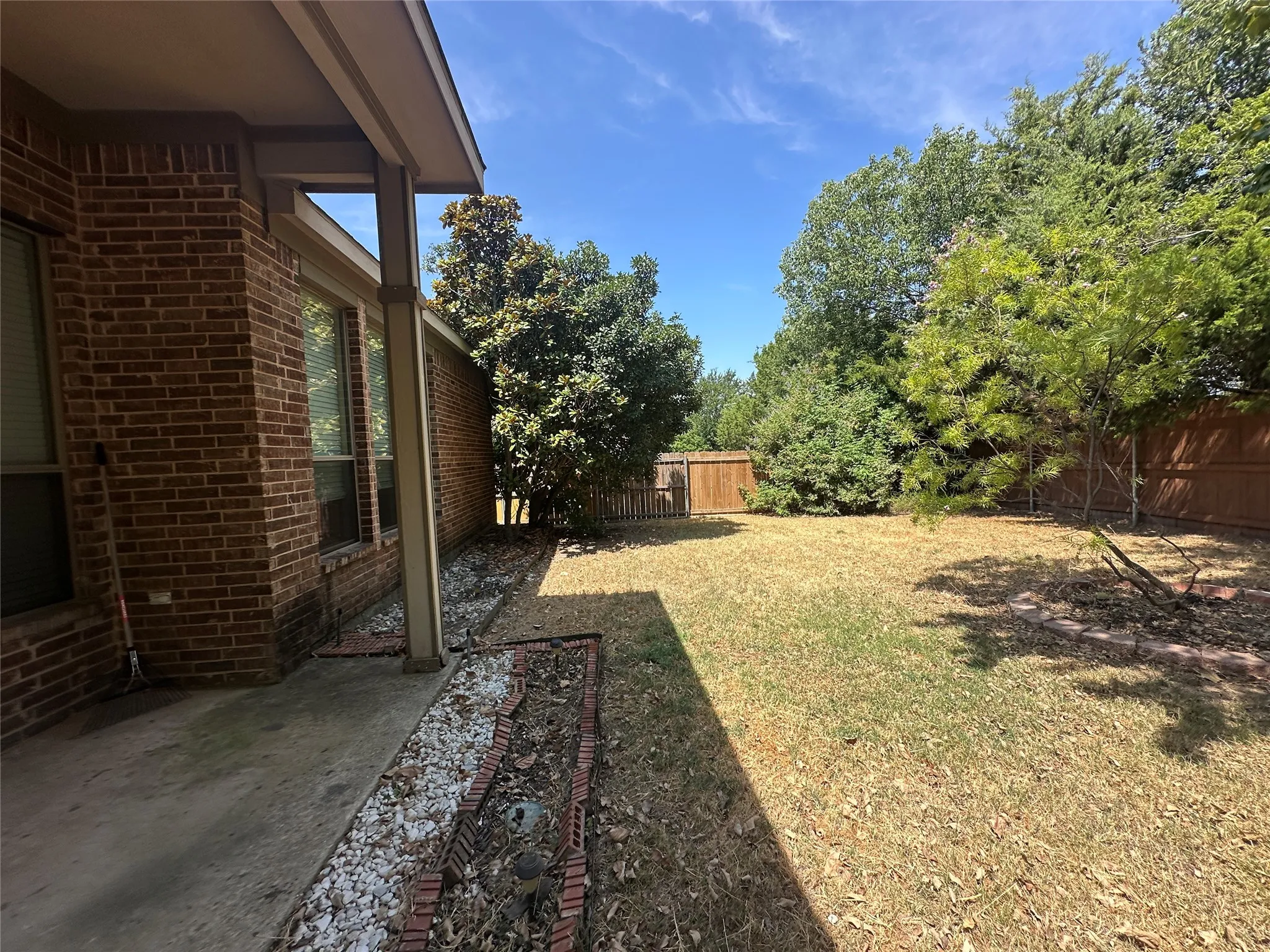 Expansive backyard featuring a wood privacy fence, mature trees, and a concrete patio