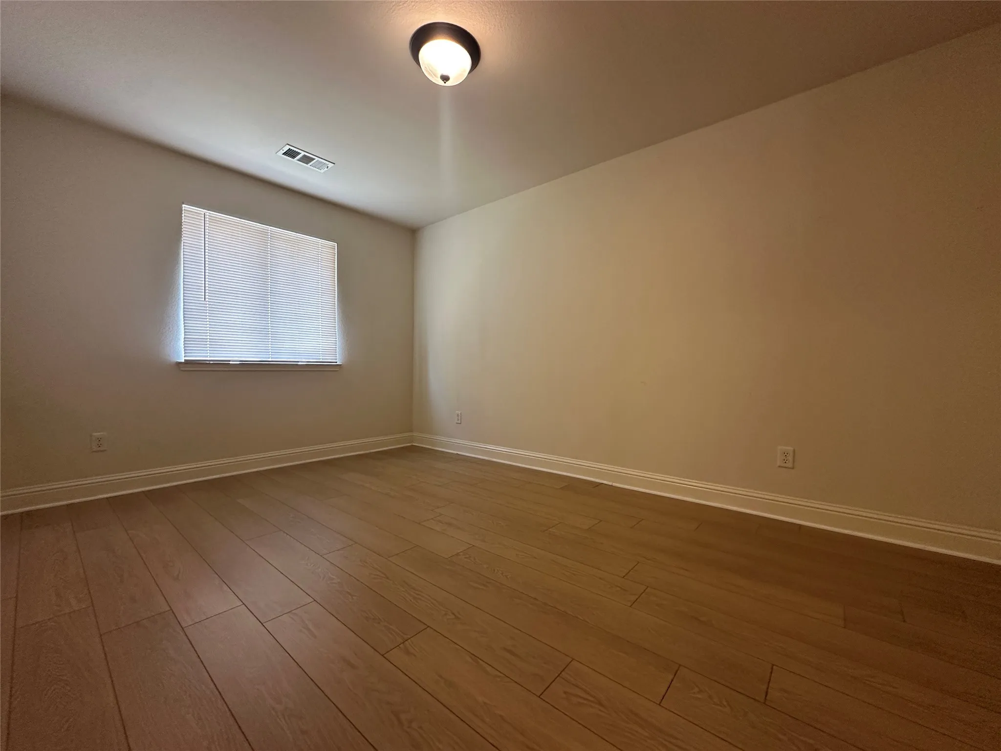 Wood-finish flooring, neutral wall tones, window with horizontal blinds, and a ceiling-mounted light fixture