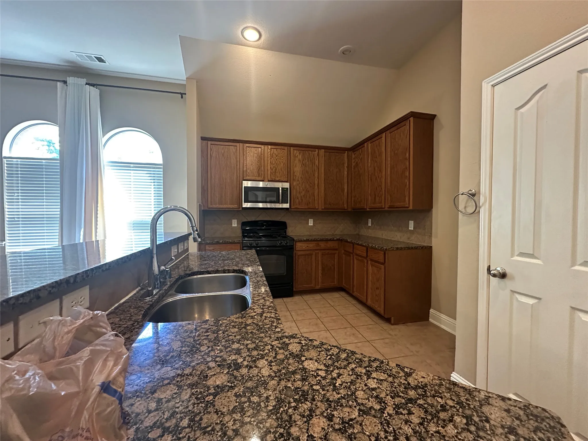 Kitchen featuring a dual basin sink with a high-arc faucet, granite-finish countertops, wood cabinetry, built-in microwave, and arched windows