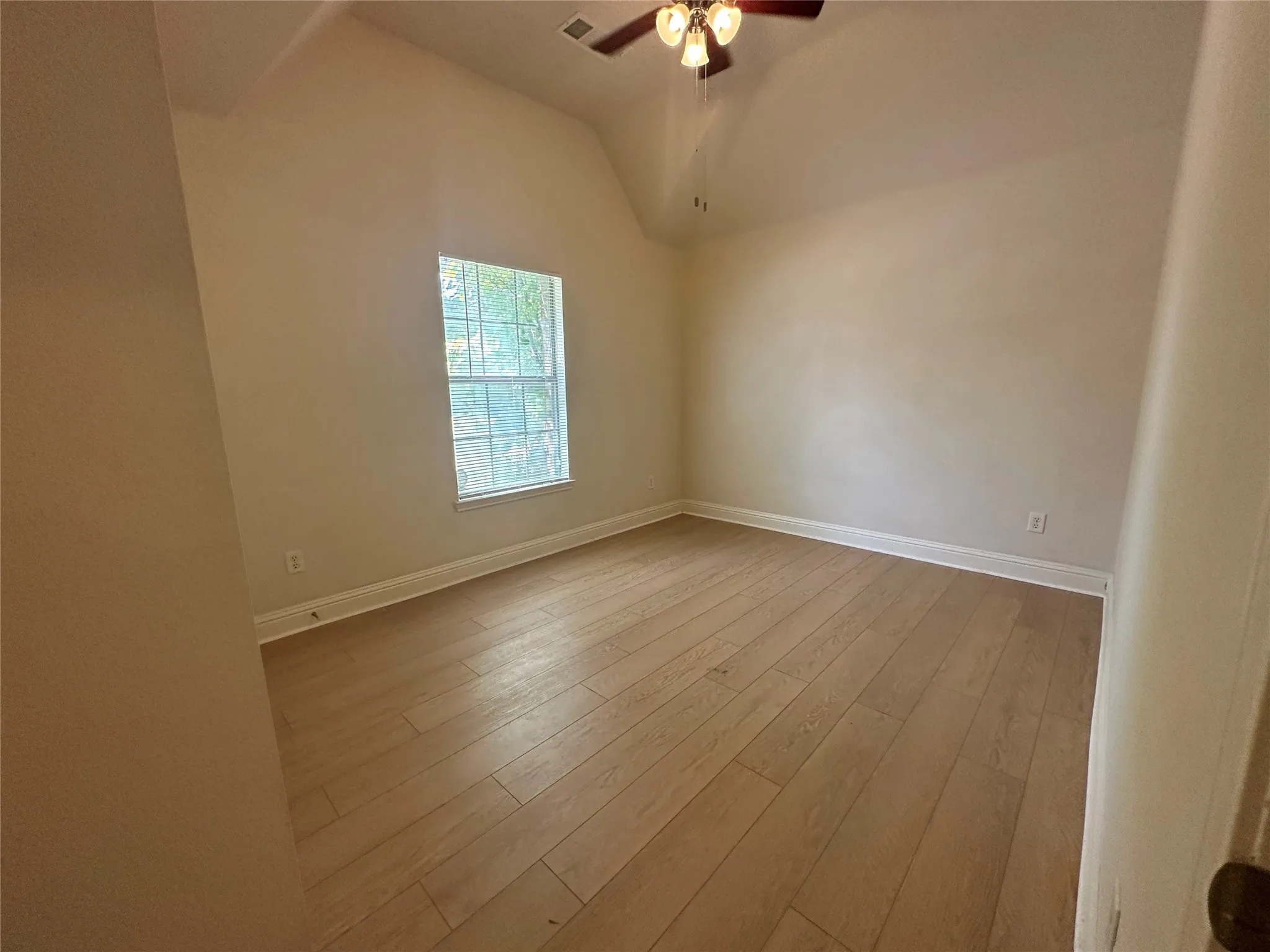 Vaulted ceiling, wood-finish flooring, single window, flush-mount ceiling fan, neutral wall tones