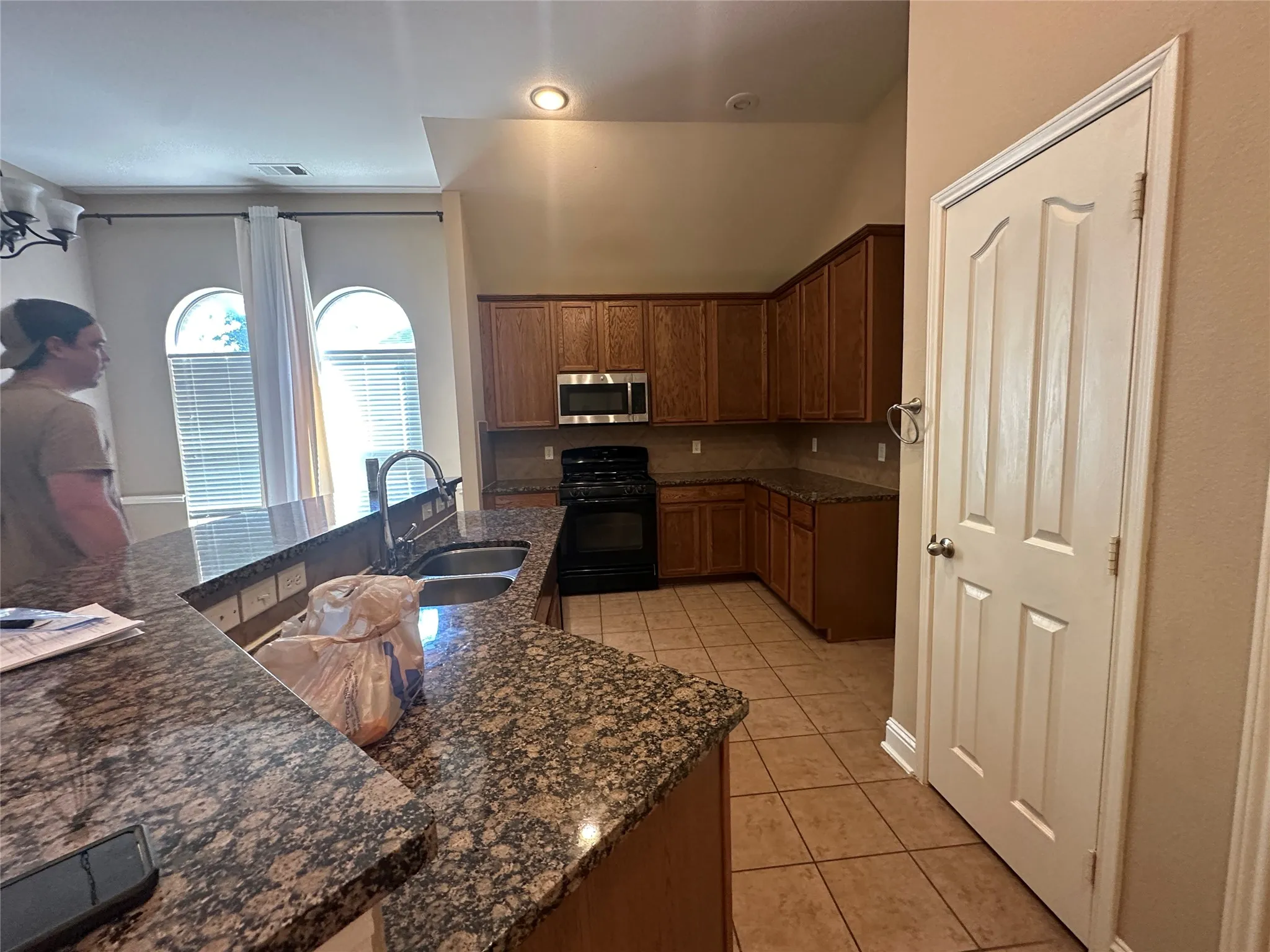 Kitchen featuring granite countertops, wood cabinetry, stainless steel microwave, black range, and tile flooring