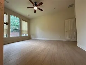 Wood-finish flooring, multiple windows, ceiling fan with integrated lighting, and a paneled interior door