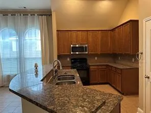 Open-concept kitchen with granite-style countertops, wood cabinetry, built-in microwave, and arched windows