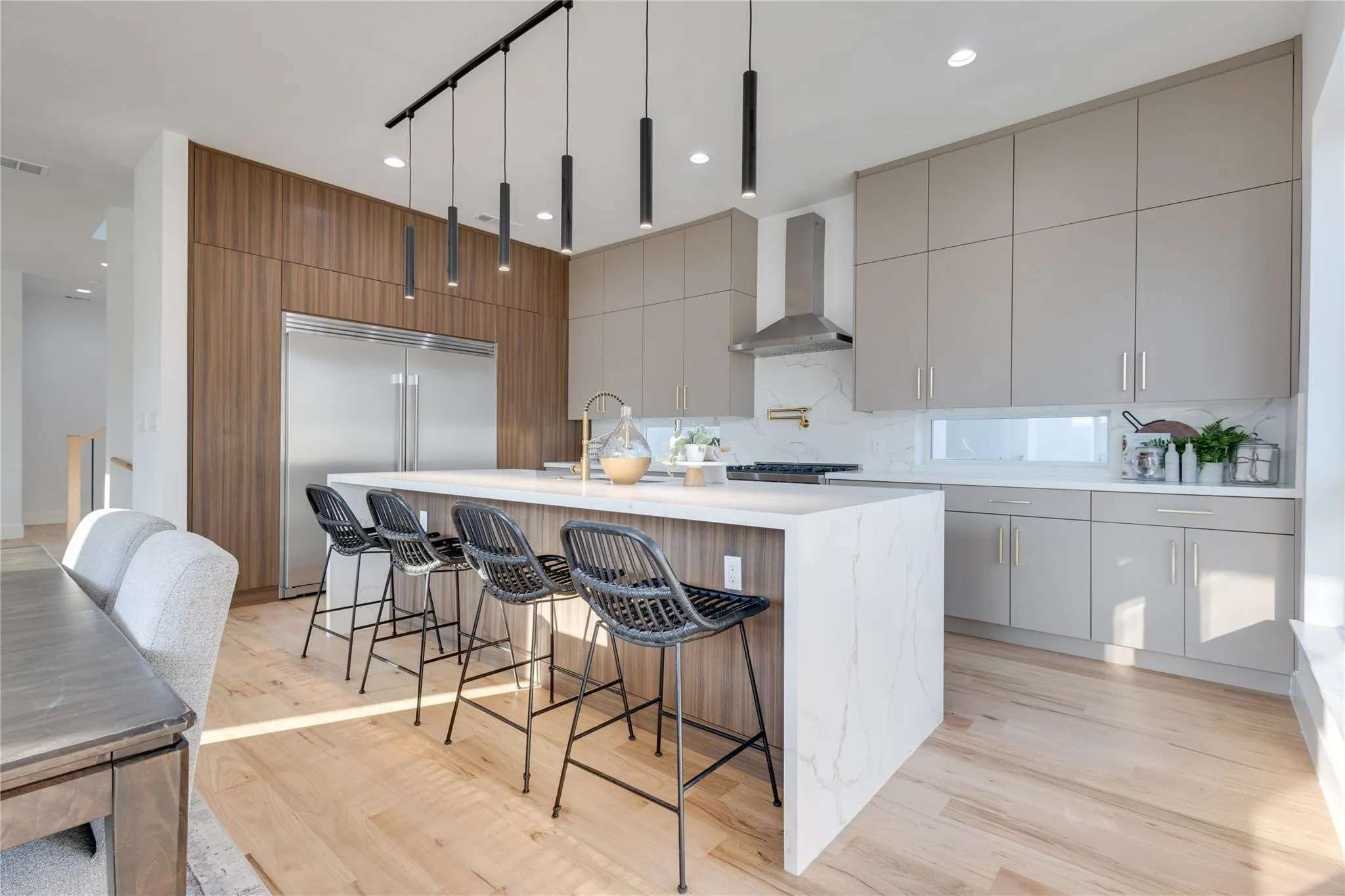 Kitchen featuring hanging light fixtures, a kitchen island with sink, stainless steel built in fridge, wall chimney range hood, and light hardwood / wood-style flooring