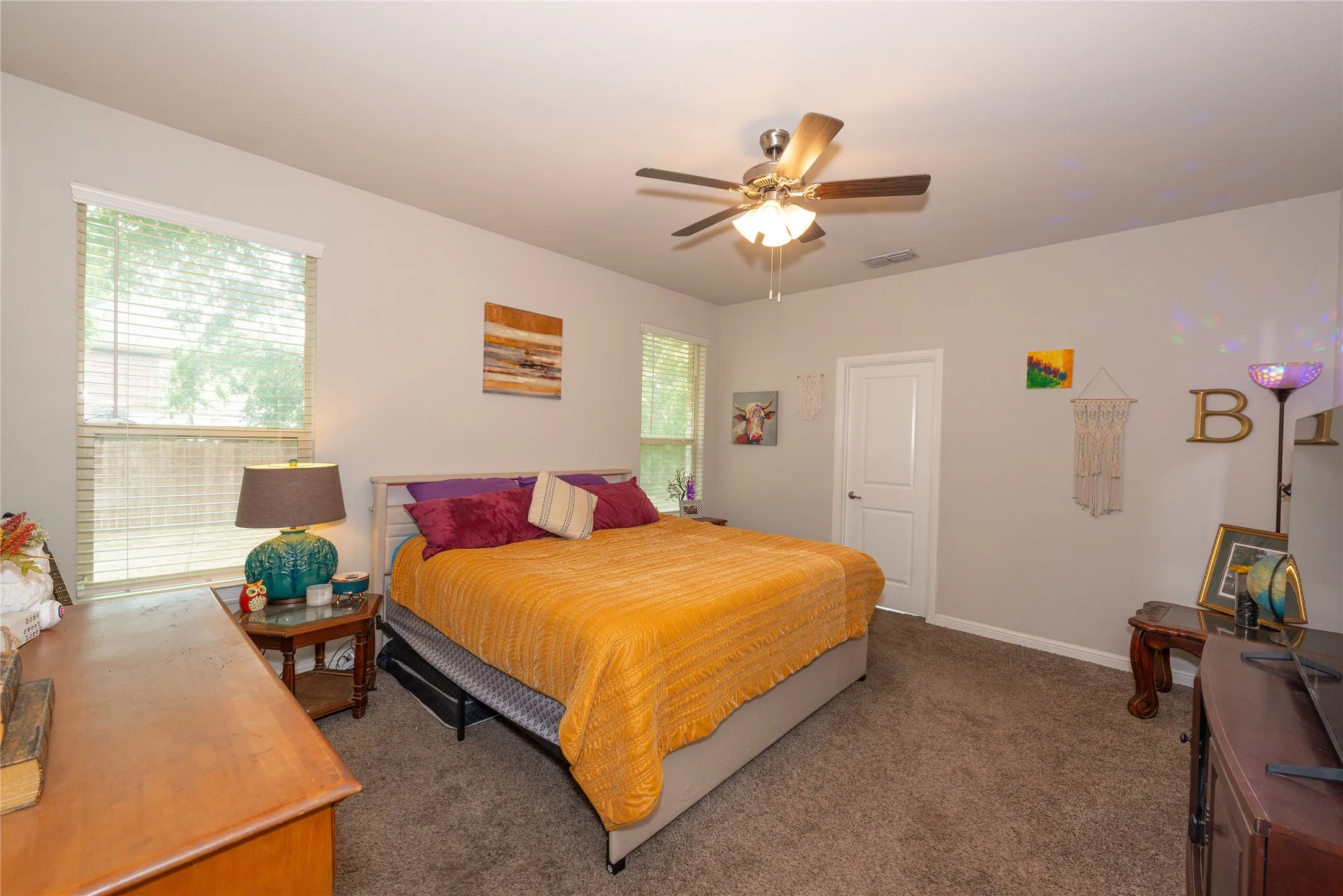 Carpeted flooring, ceiling fan, white paneled door, and multiple windows with blinds
