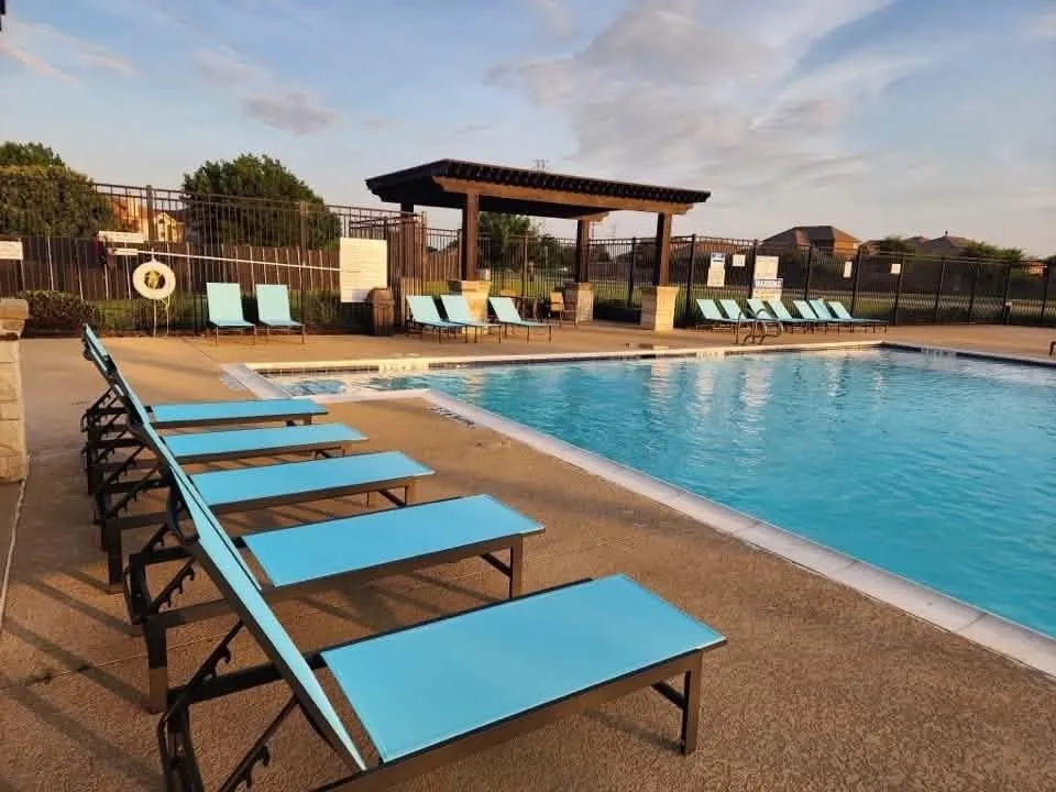 Expansive outdoor swimming pool with integrated seating, concrete decking, and a shaded pergola structure
