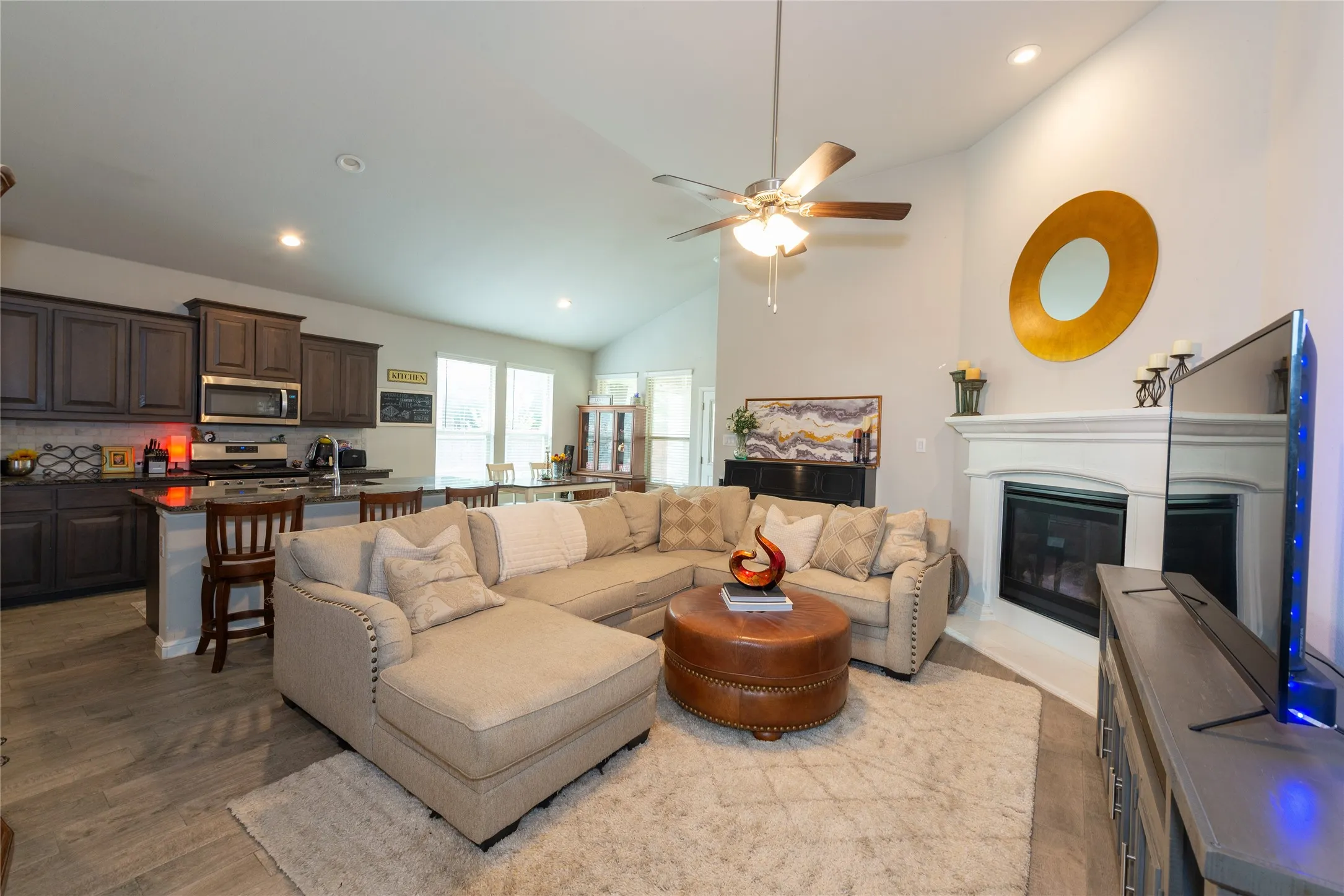 Vaulted ceiling with a ceiling fan, recessed lighting, wood-finish flooring, and a fireplace with a white mantel