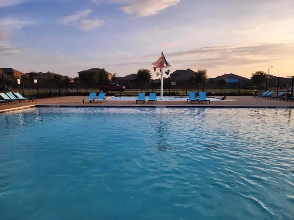 Expansive outdoor pool area featuring a large swimming pool, concrete decking, and a separate wading pool with a water feature