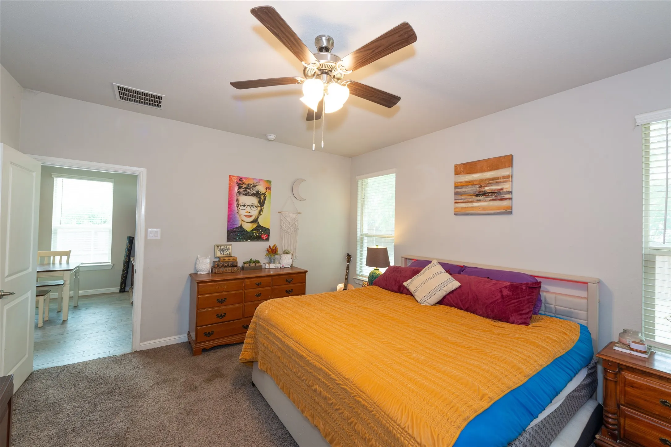 Carpeted flooring, ceiling fan with integrated lighting, multiple windows with blinds, and light-toned wall paint