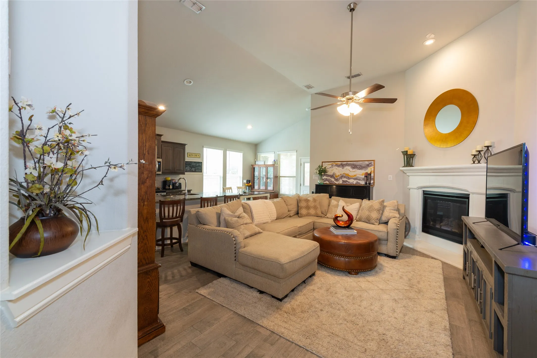 Vaulted ceiling with a ceiling fan, fireplace with a white mantel, and wood-finish flooring