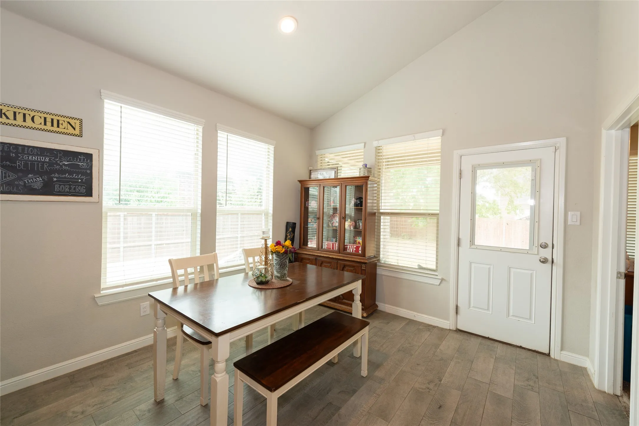 Vaulted ceiling, recessed lighting, wood-finish flooring, multiple windows with blinds, and a rear exterior door with a glass insert